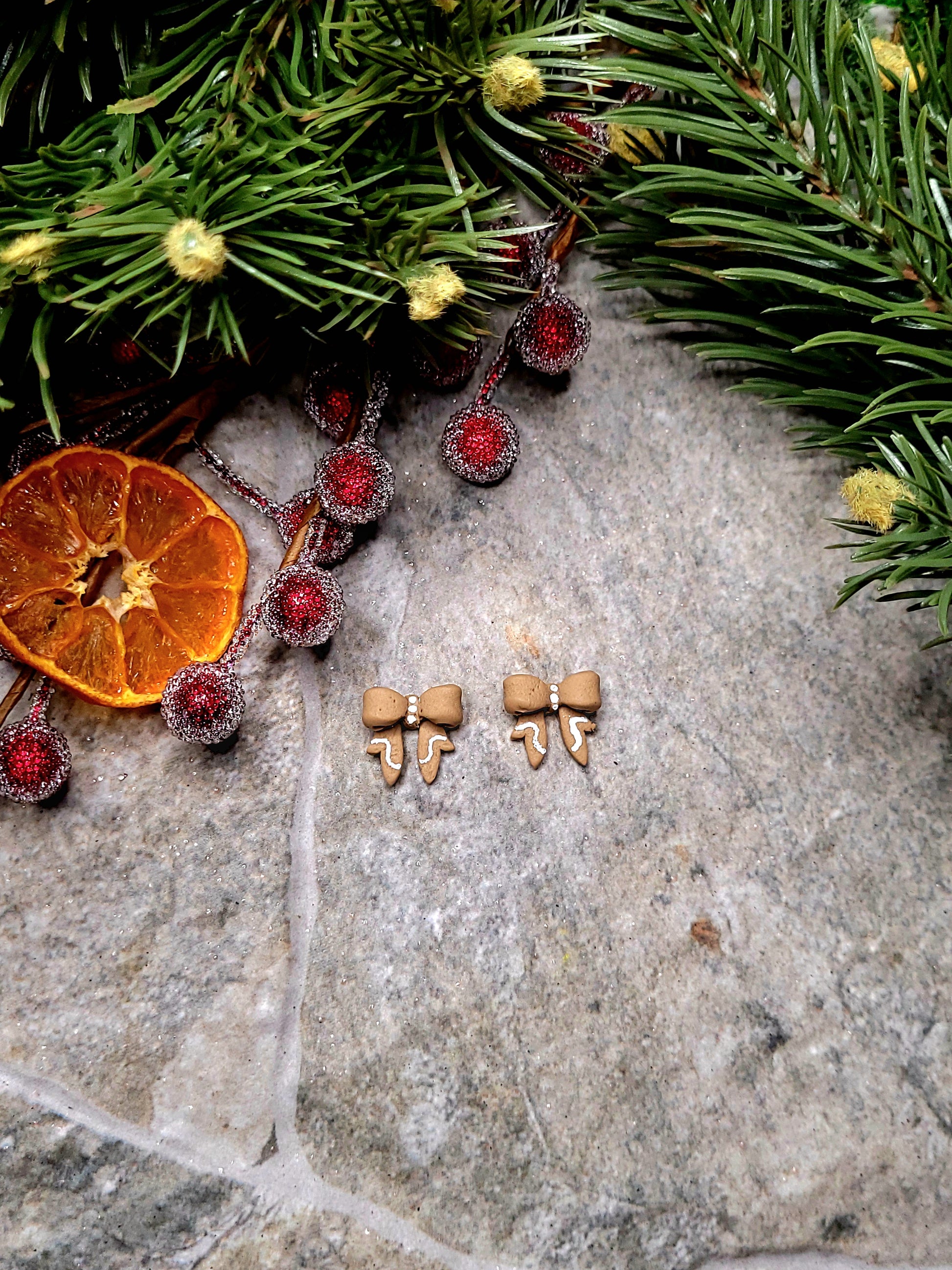 Gingerbread Bow studs on a stone background surrounded by foliage