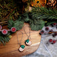 yule log earrings on a wood and stone background surrounded by foliage. 