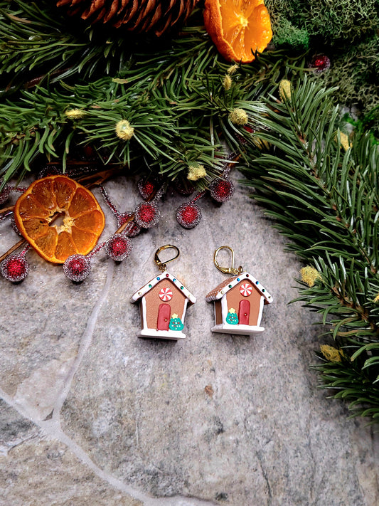 Gingerbread house earrings on a stone background surrounded by foliage. 