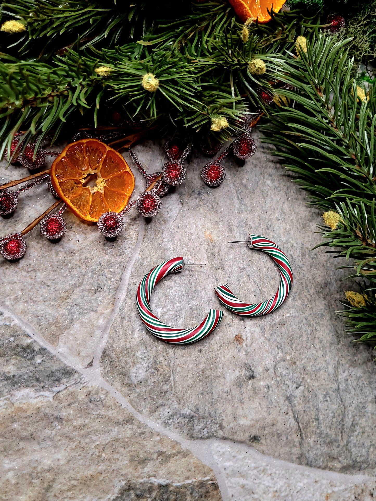 Retro Candy Cane Hoop Earring on a  stone background surrounded by foliage. 