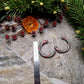 Retro Candy Cane Hoop Earring next to a ruler on a  stone background surrounded by foliage. 