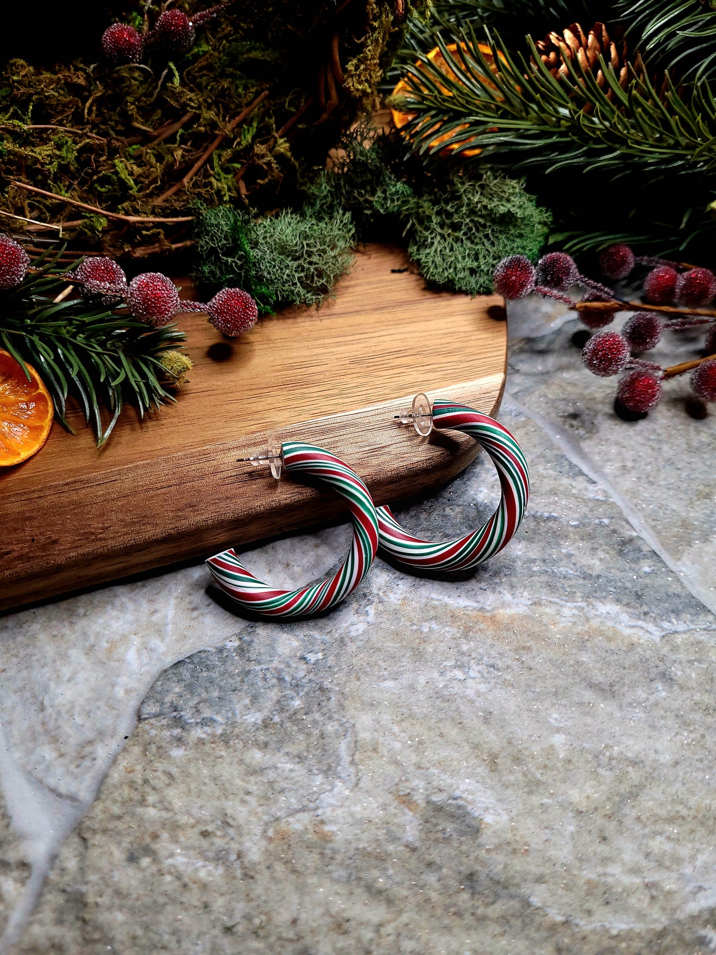 Retro Candy Cane Hoop Earring on a  wood and stone background surrounded by foliage. 