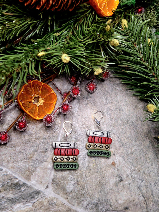 Retro Christmas Bookstack Earring on a stone background surrounded by foliage. 