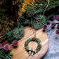 Holiday Wreath Necklace on a stone background surrounded by foliage. 