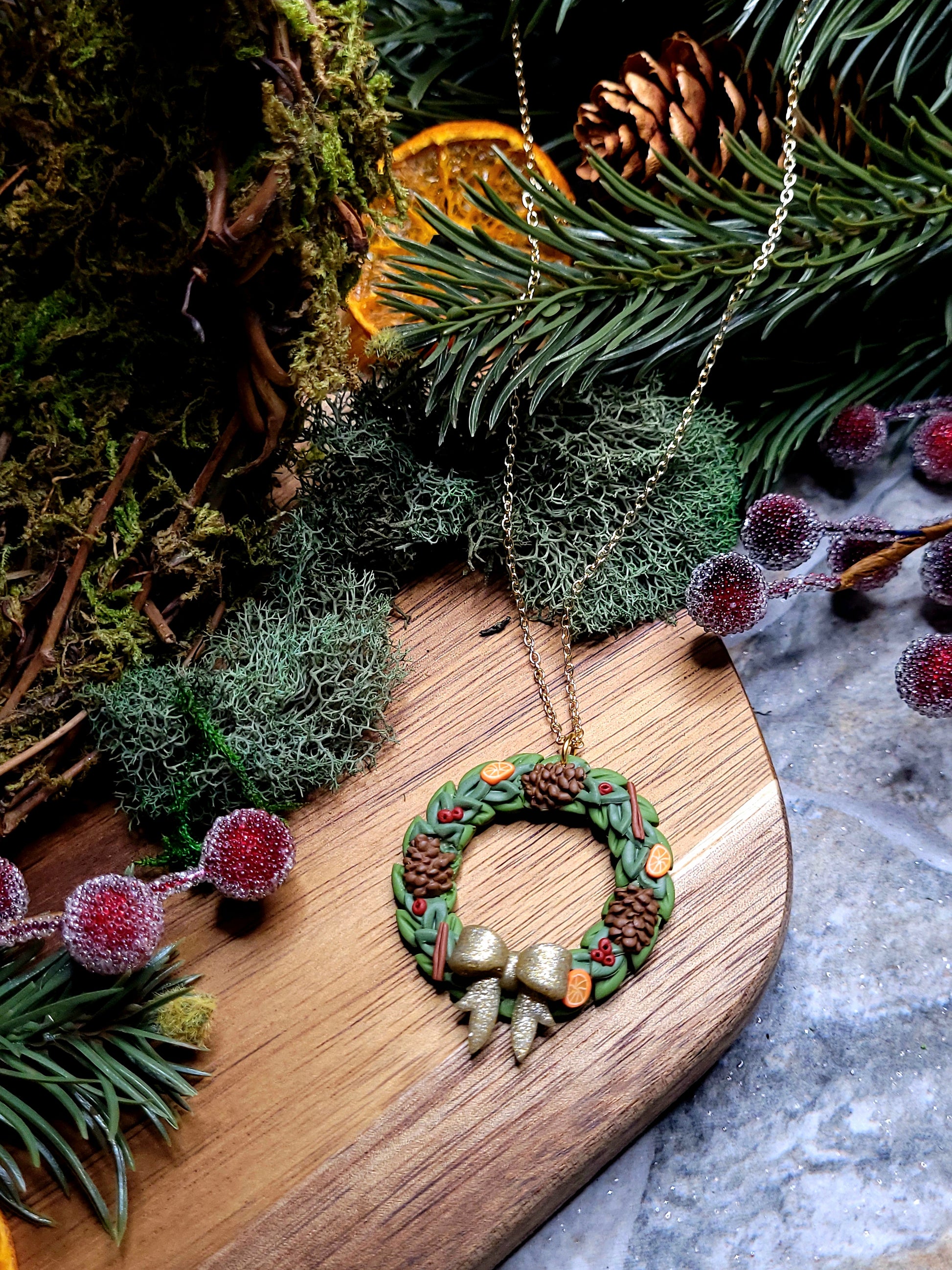 Holiday Wreath Necklace on a stone background surrounded by foliage. 