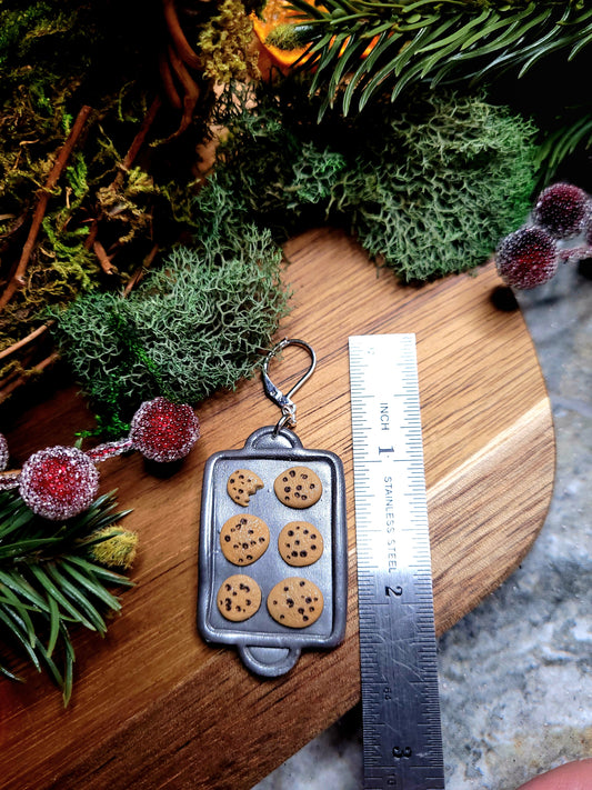 Cookie Tray earring next to ruler on a  wood and stone background surrounded by foliage