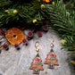 Christmas Tree Shelf Earring on a stone background surrounded by foliage. 