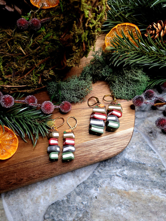 Festive Bookstack Earring on a wood and stone background surrounded by foliage. 