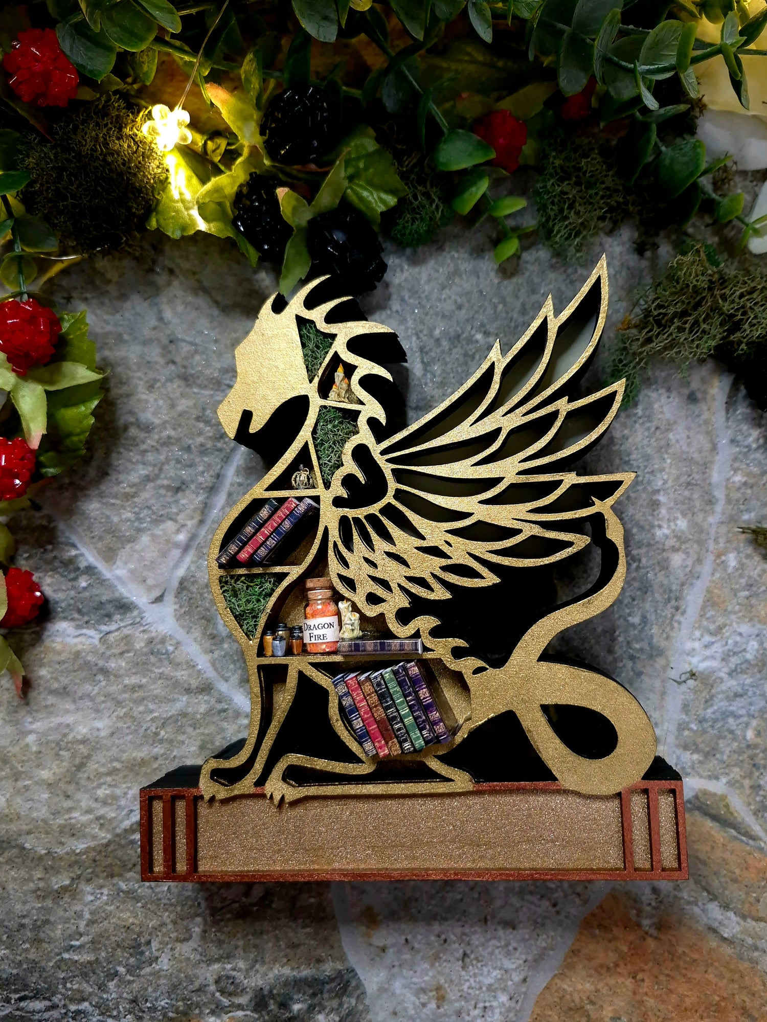 Gold dragon mini bookcase on a stone background surrounded by foliage.