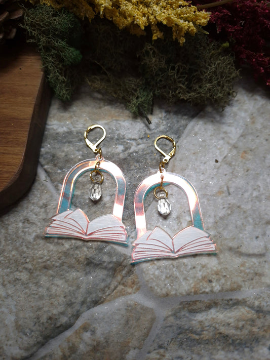 Open Book Arch earrings on a stone background surrounded by foliage 

