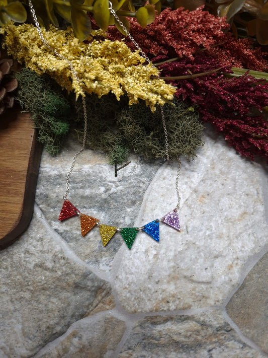 Necklace with colorful triangle pendants on a stone surface with plants in the background