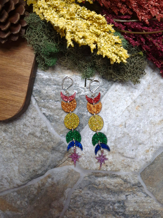 Rainbow moon phase earrings on a stone background surrounded by foliage 
