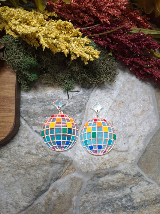 close up of Colorful disco ball earrings on a stone surface with decorative plants.