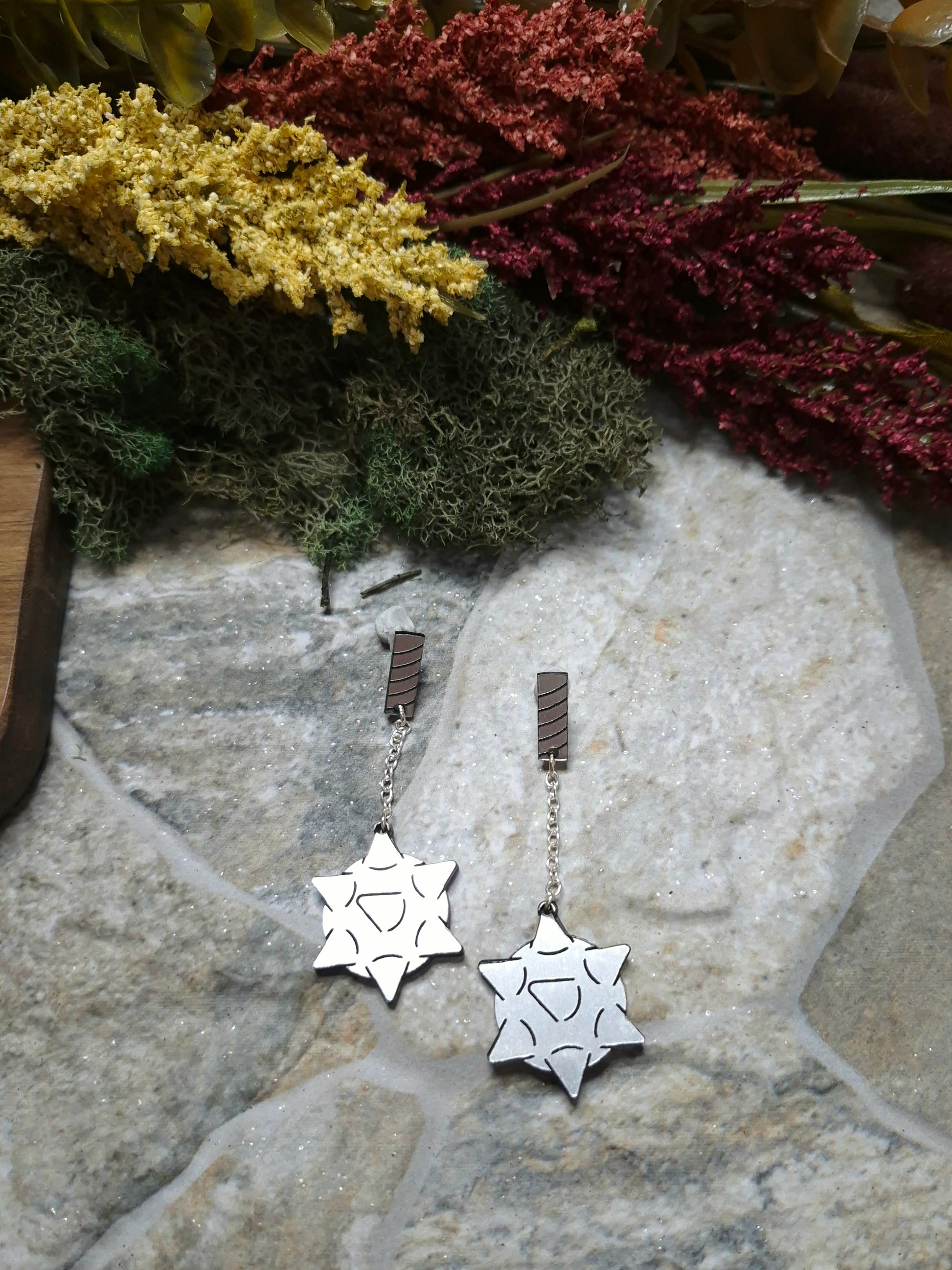 flail earrings on a stone background surrounded by foliage. 