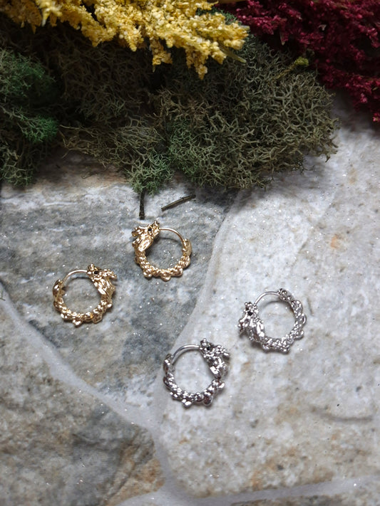 Gold and Silver dragon hoop earrings on a stone background surrounded by foliage