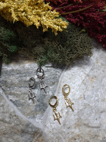Gold and Silver trident earrings on a stone background surrounded by foliage