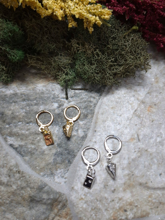 Gold and Silver cheese wedge earrings on a stone background surrounded by foliage