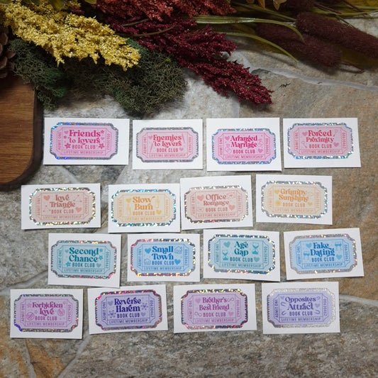 Book Trope Stickers on a stone background surrounded by foliage. 