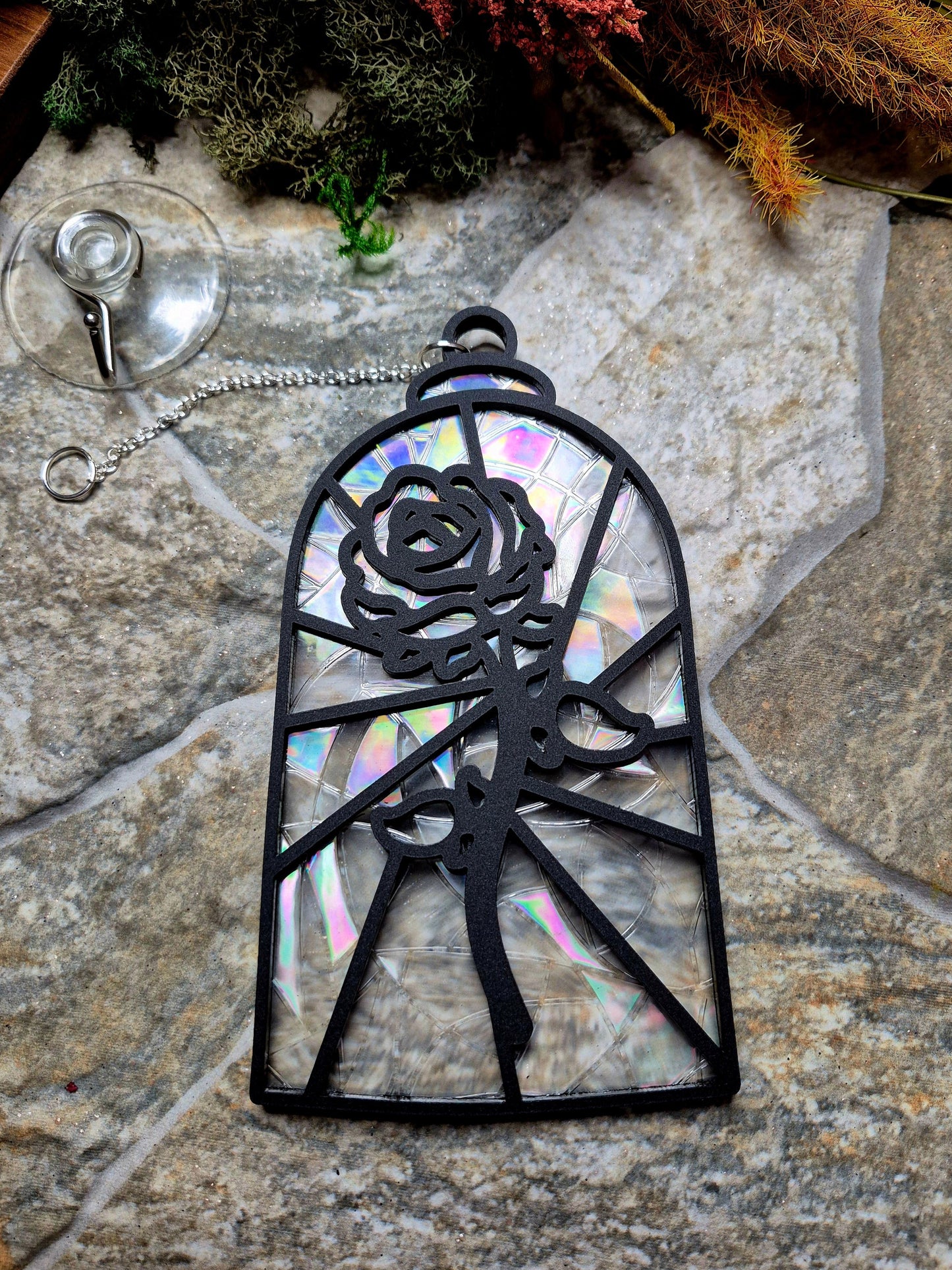 Enchanted rose suncatcher on a stone background surrounded by foliage 
