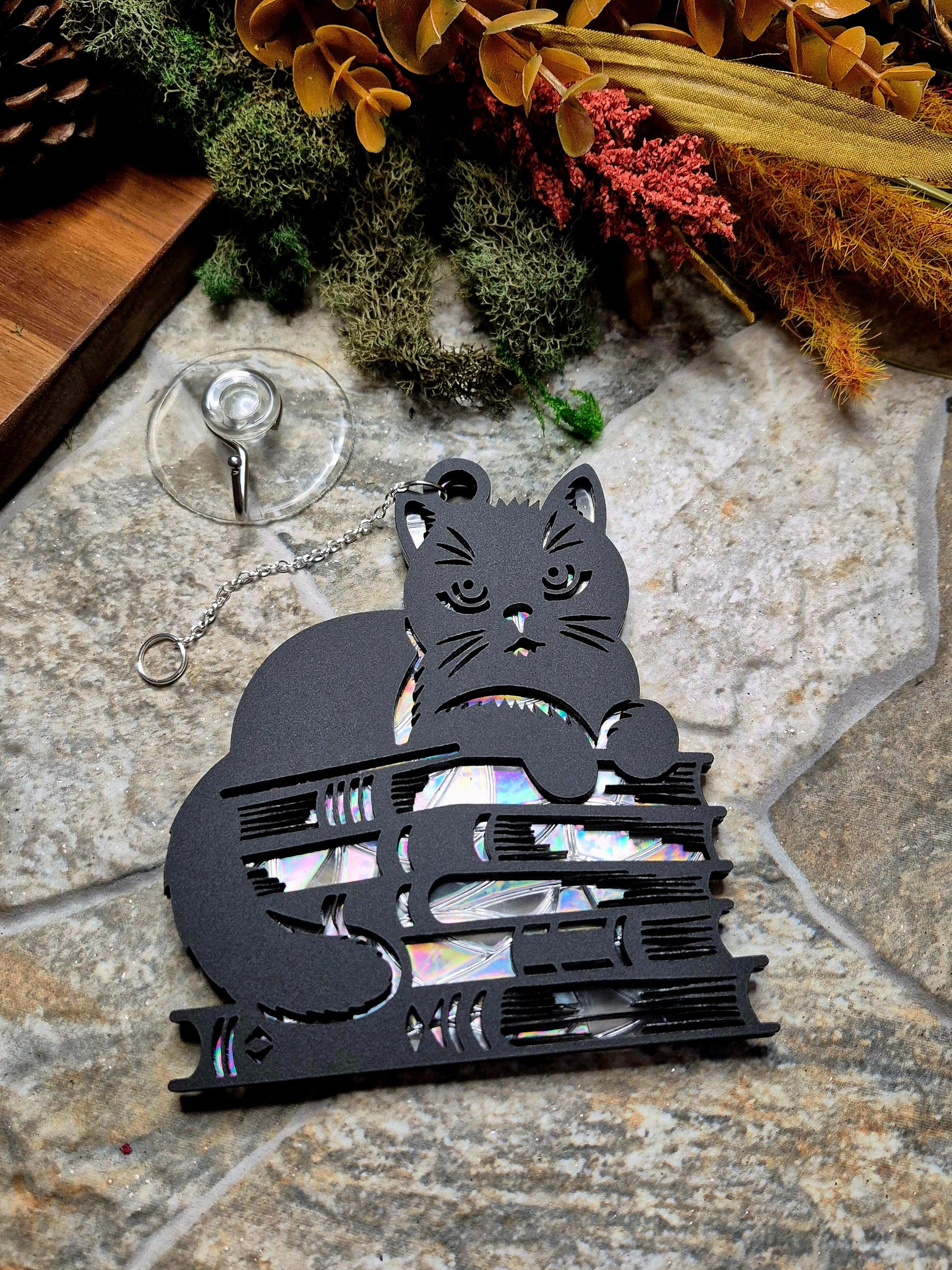 Book cat suncatcher on a stone background surrounded by foliage
