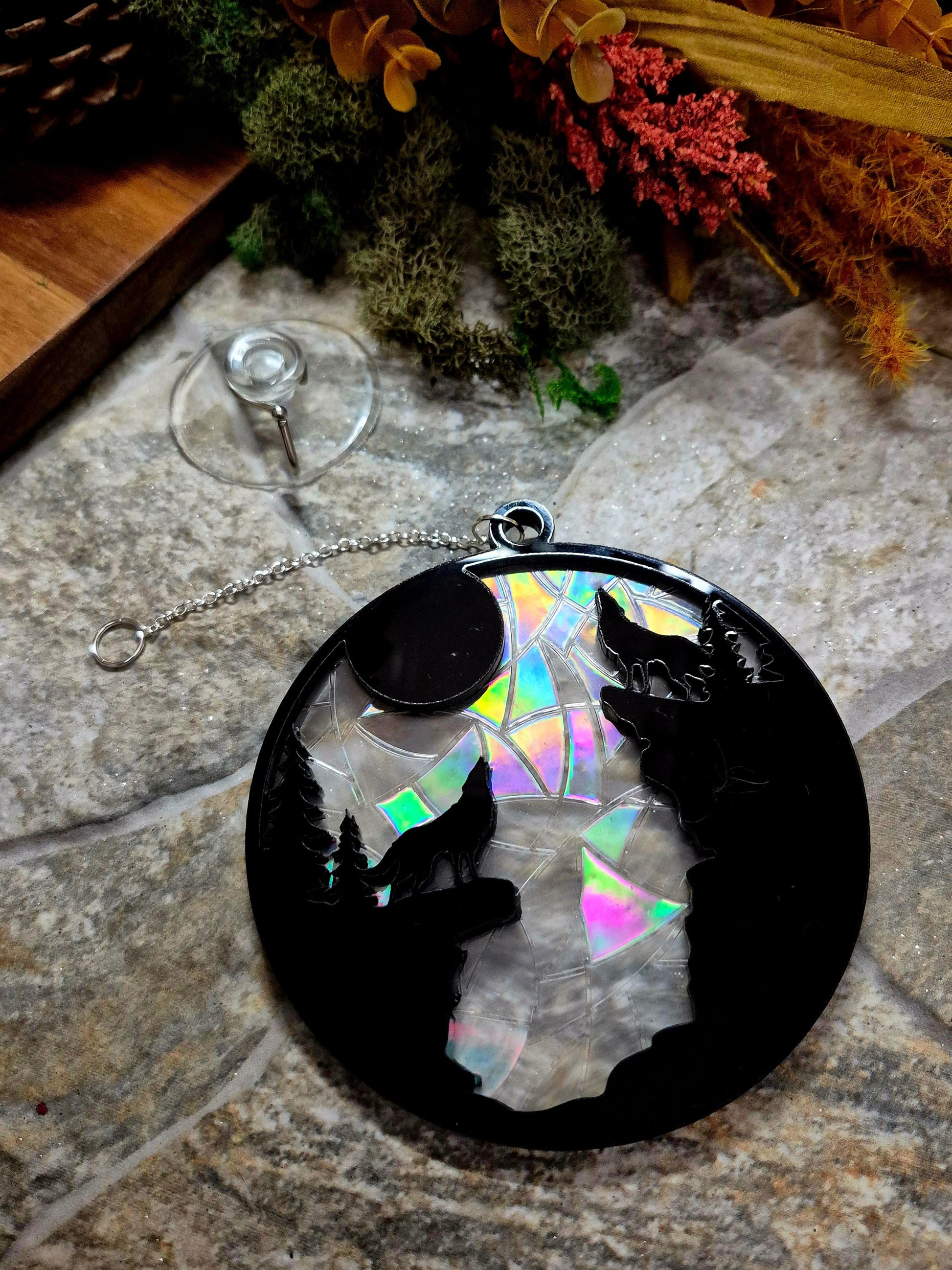 Howl at the Moon suncatcher on a stone background surrounded by foliage 
