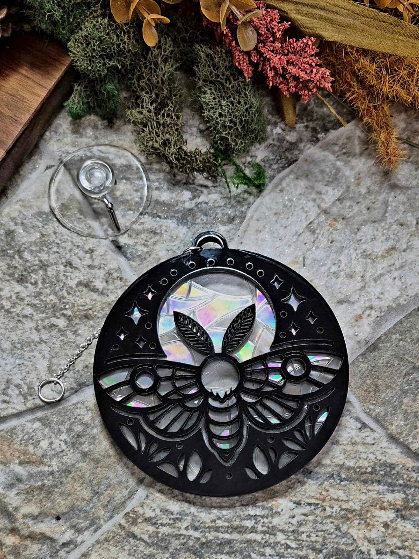 Celestial Moth suncatcher on a stone background surrounded by foliage 

