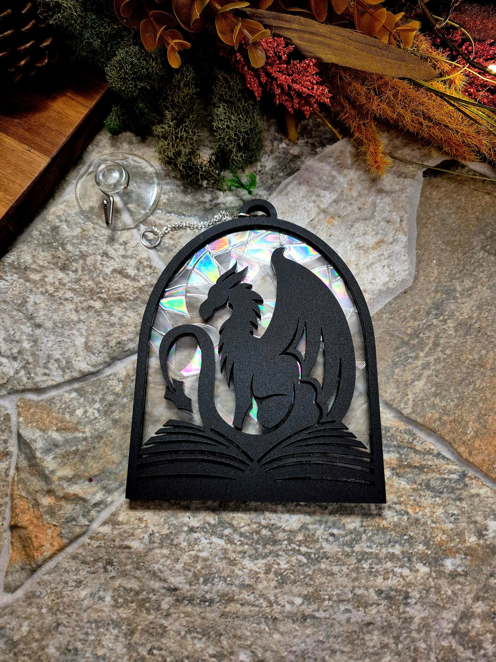 Book Dragon suncatcher on a stone background surrounded by foliage
