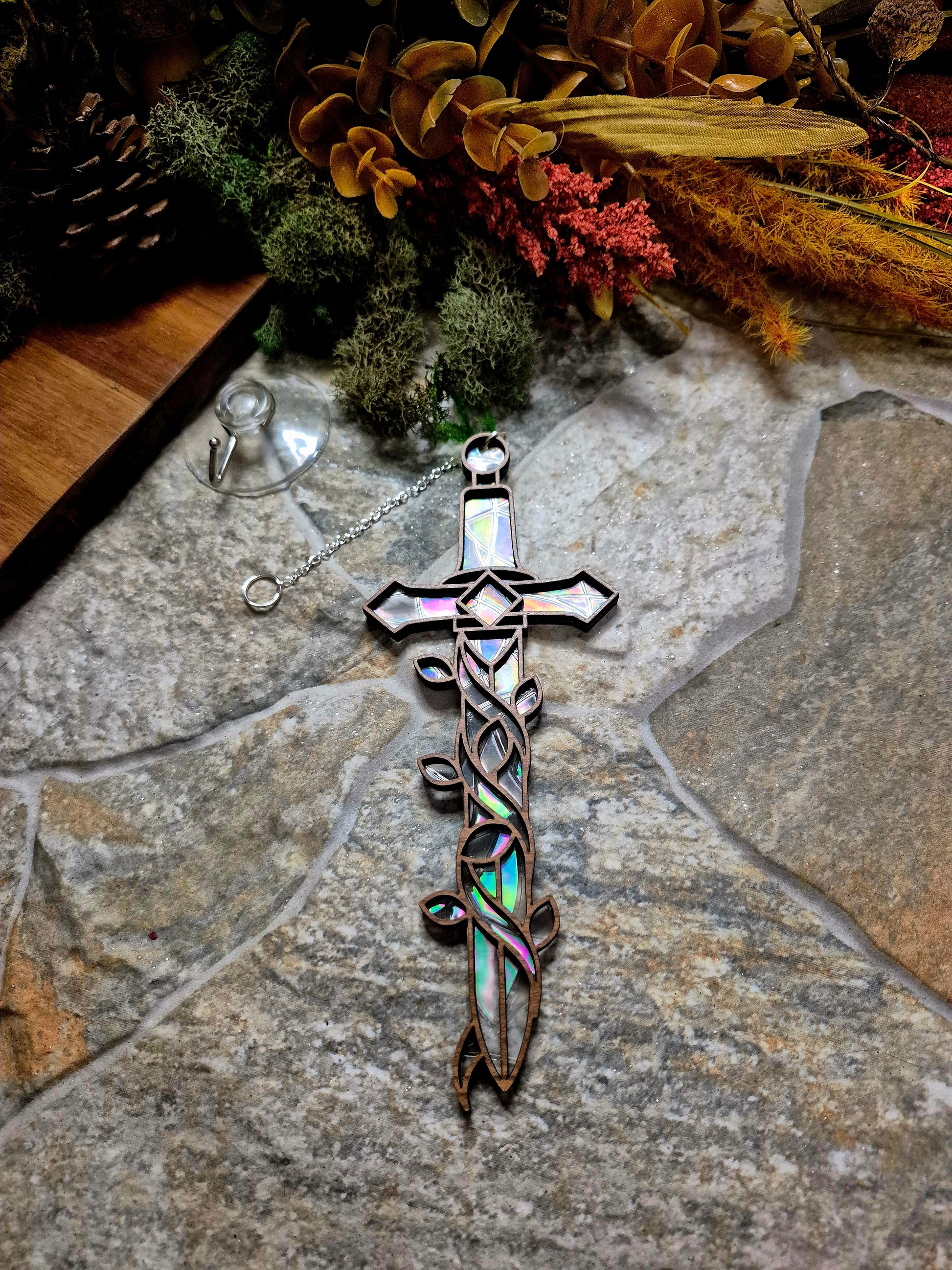 Enchanted sword suncatcher on a stone background surrounded by foliage 
