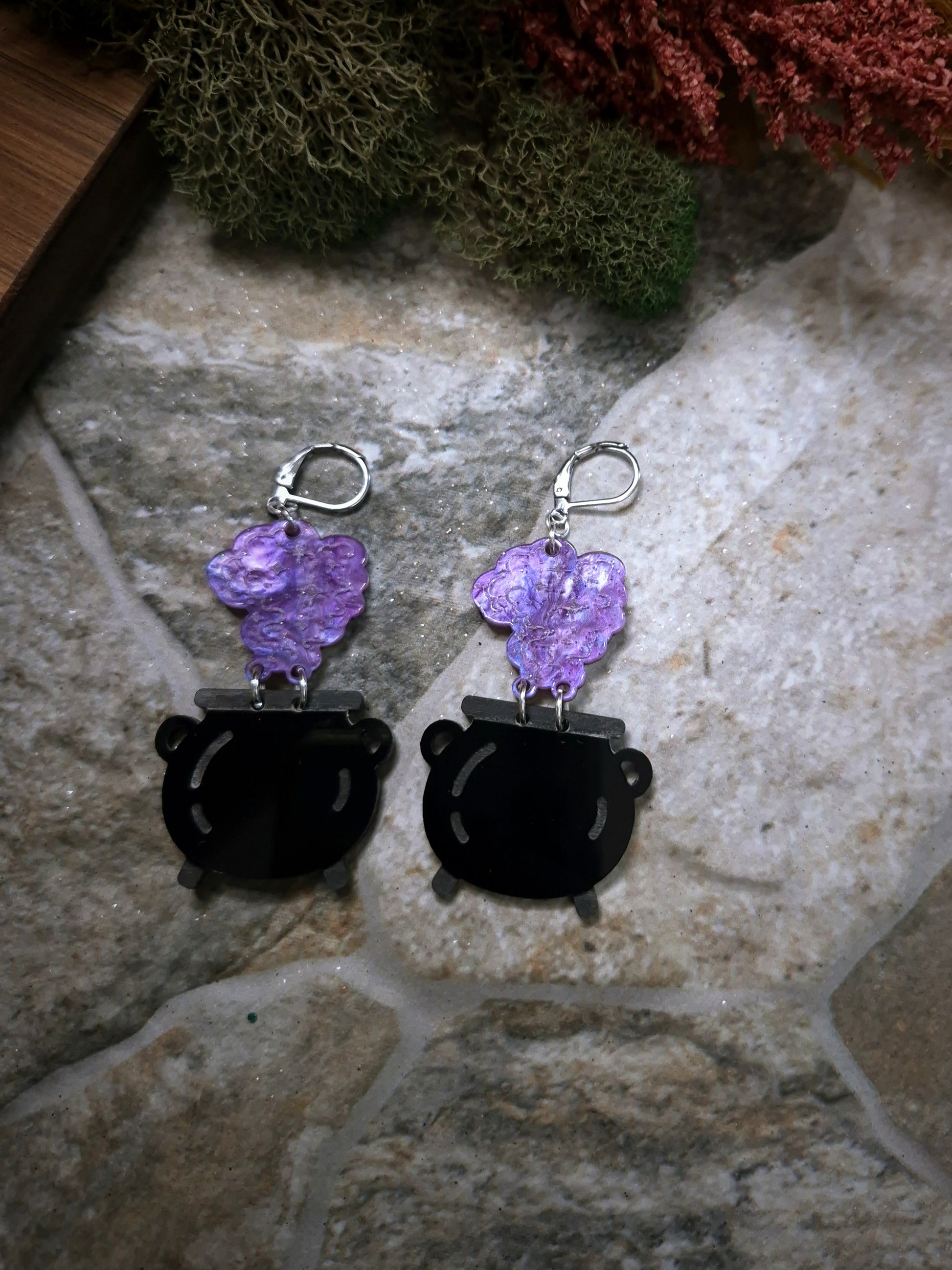 close up of Cauldron earrings on a stone and wood background surrounded by foliage 
