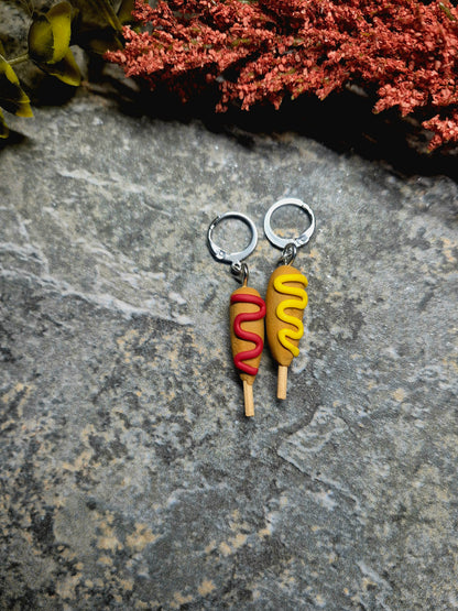 corn dog earrings on a stone background surrounded by foliage 
