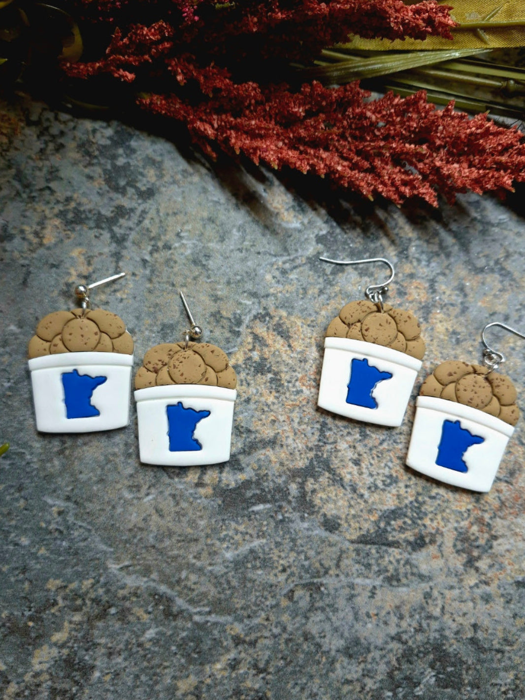 State fair cookie bucket earrings on a stone background surrounded by foliage .