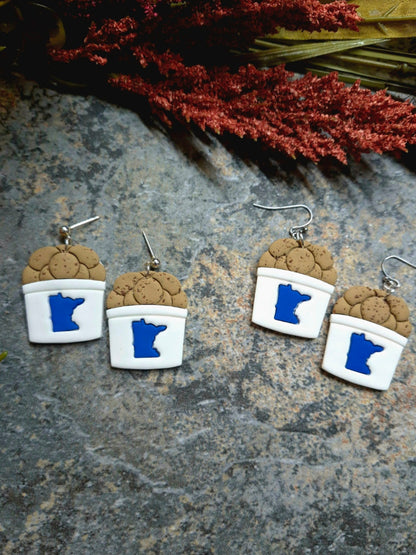 State fair cookie bucket earrings on a stone background surrounded by foliage .