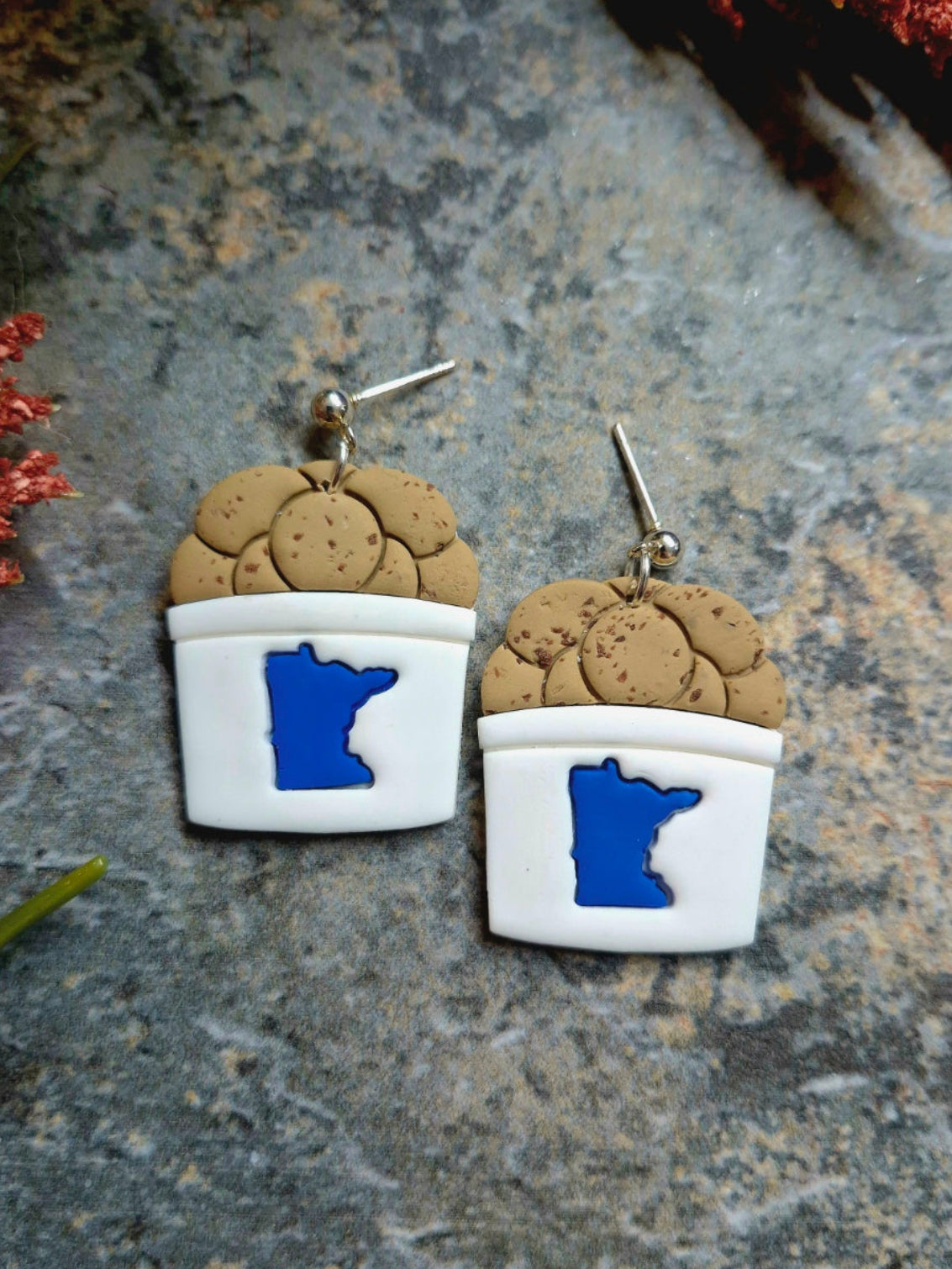close up of stud State fair cookie bucket earrings on a stone background surrounded by foliage .