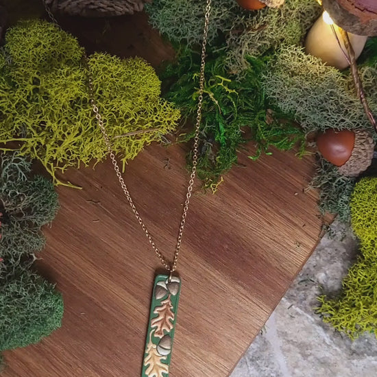 video close up of the Green bar shaped pendant with metallic acorns and oak leaves.