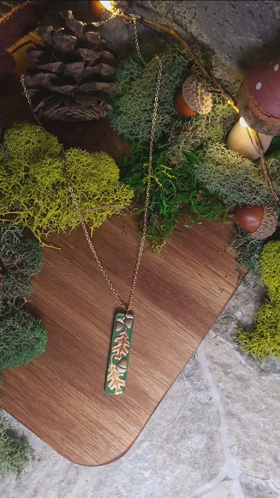 video close up of the Green bar shaped pendant with metallic acorns and oak leaves.