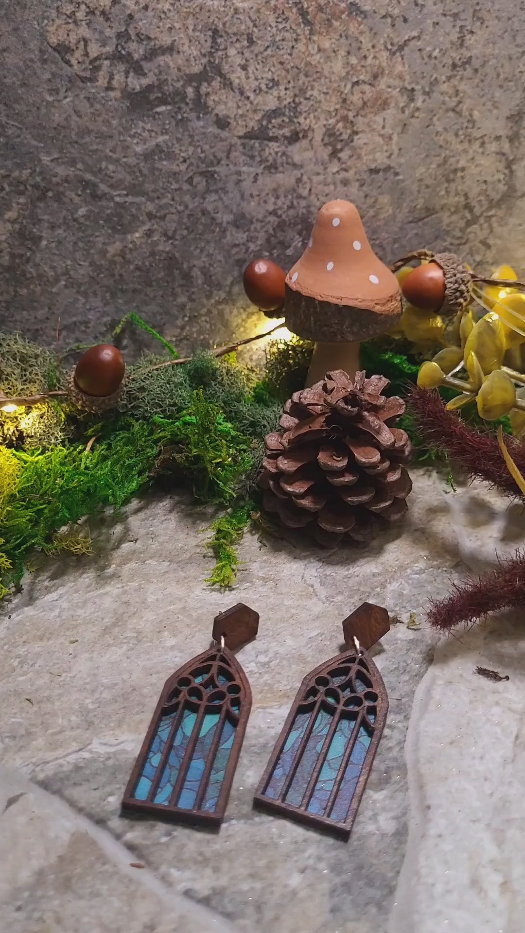 video close up of cathedral window earrings on a stone background surrounded by foliage.