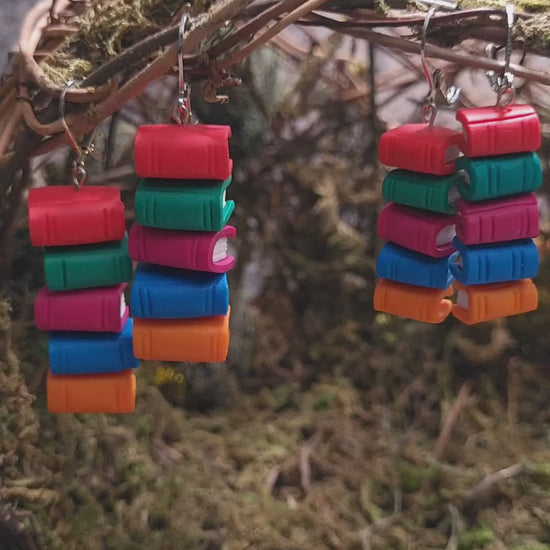 video close up of Bookstack earrings made of polymer clay in two sizes sits on a mossy background 