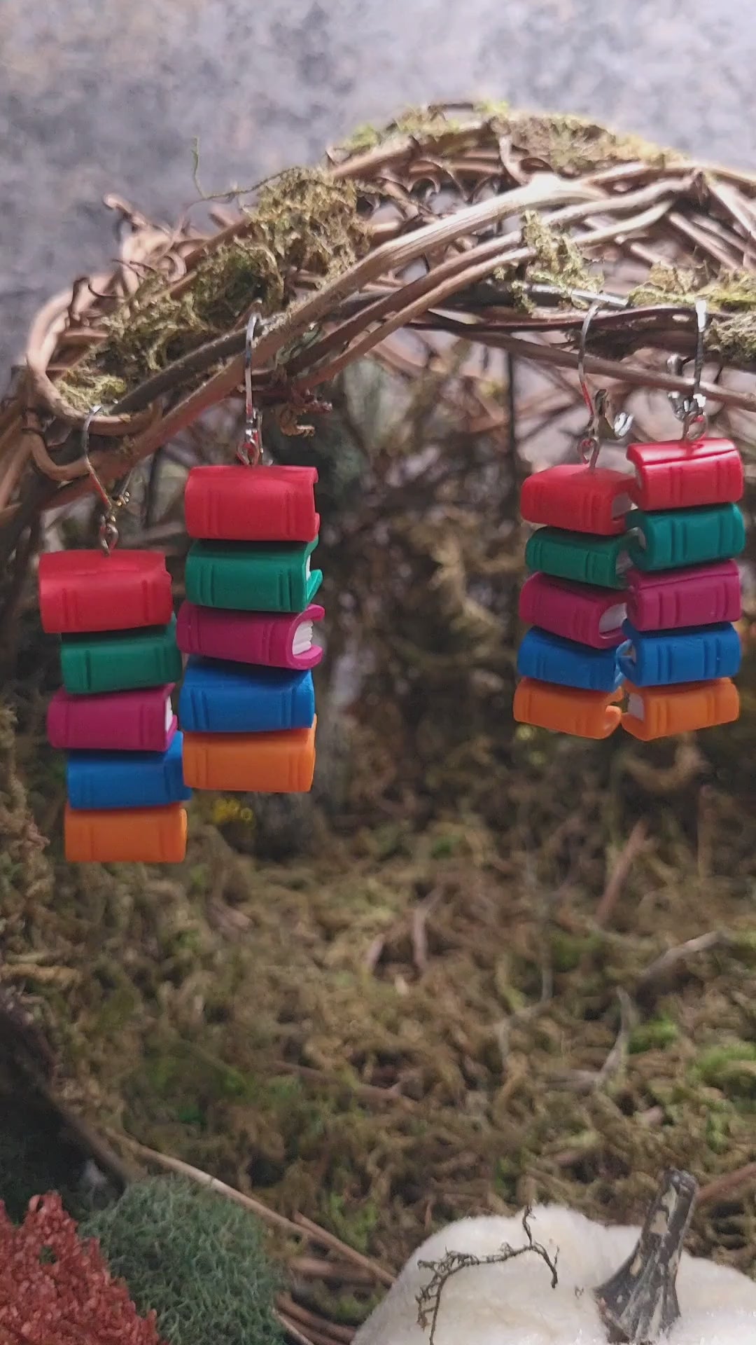 video close up of Bookstack earrings made of polymer clay in two sizes sits on a mossy background 