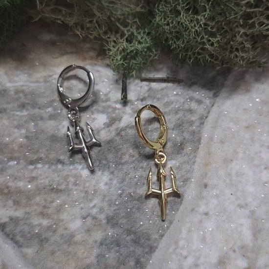 video of Gold and Silver trident earrings on a stone background surrounded by foliage