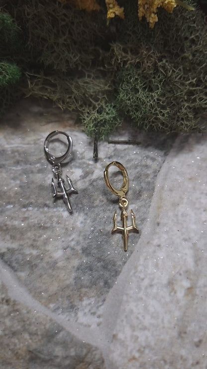 video of Gold and Silver trident earrings on a stone background surrounded by foliage