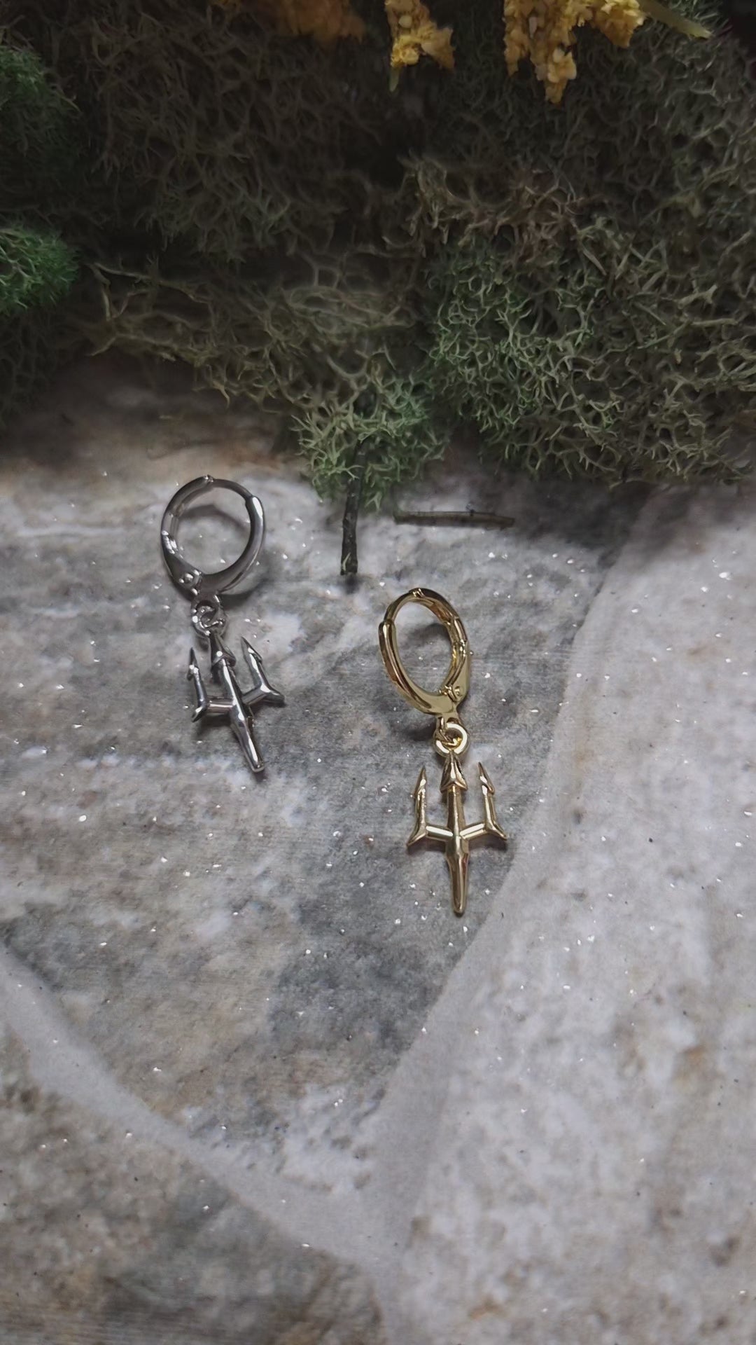 video of Gold and Silver trident earrings on a stone background surrounded by foliage