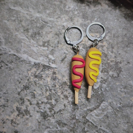 video of corn dog earrings on a stone background surrounded by foliage 
