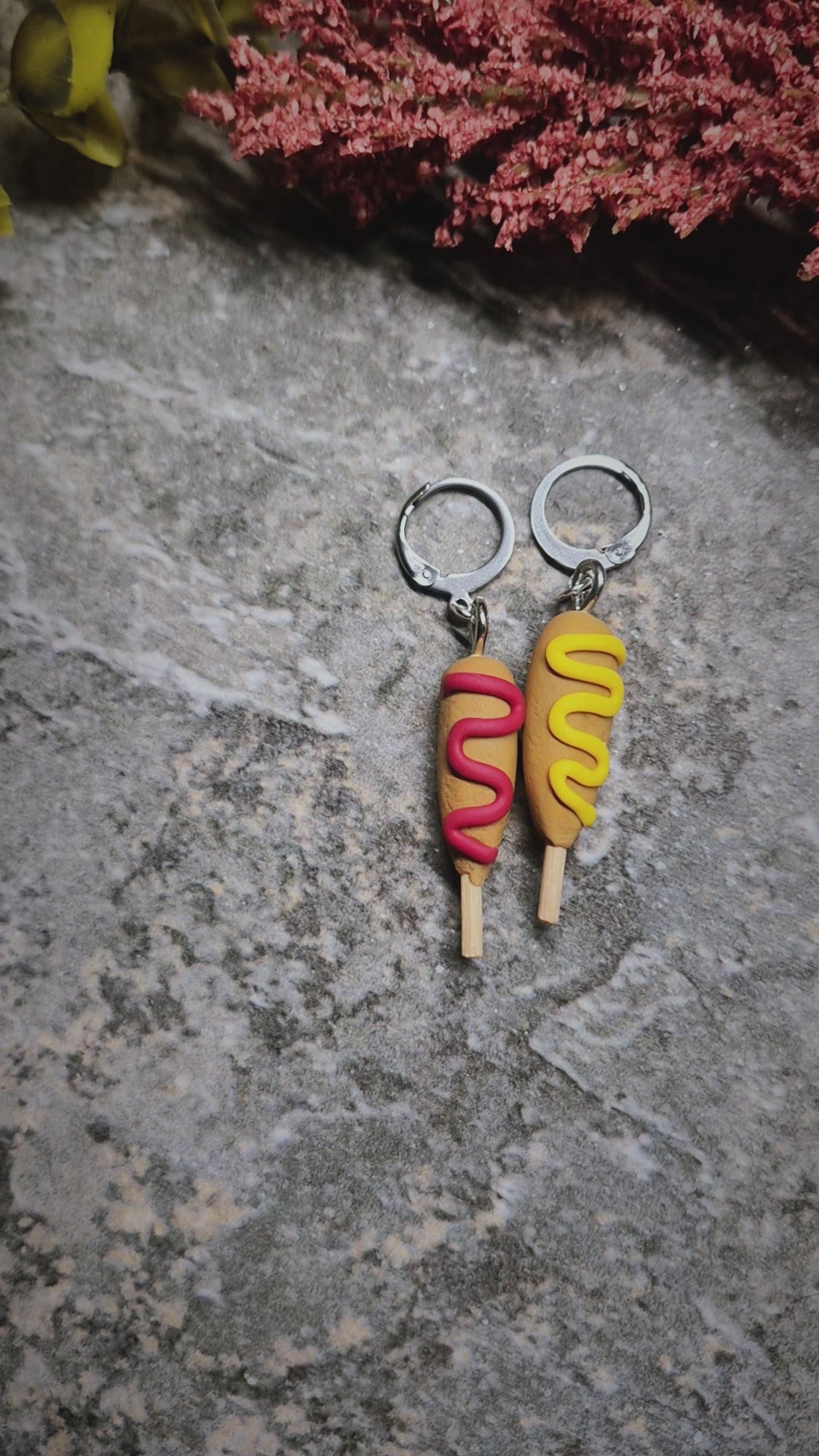 video of corn dog earrings on a stone background surrounded by foliage 
