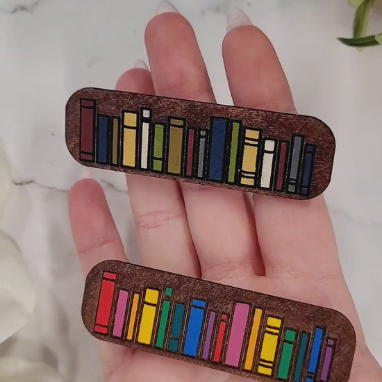 video close up of book hair clips on a white marble background surrounded by foliage.