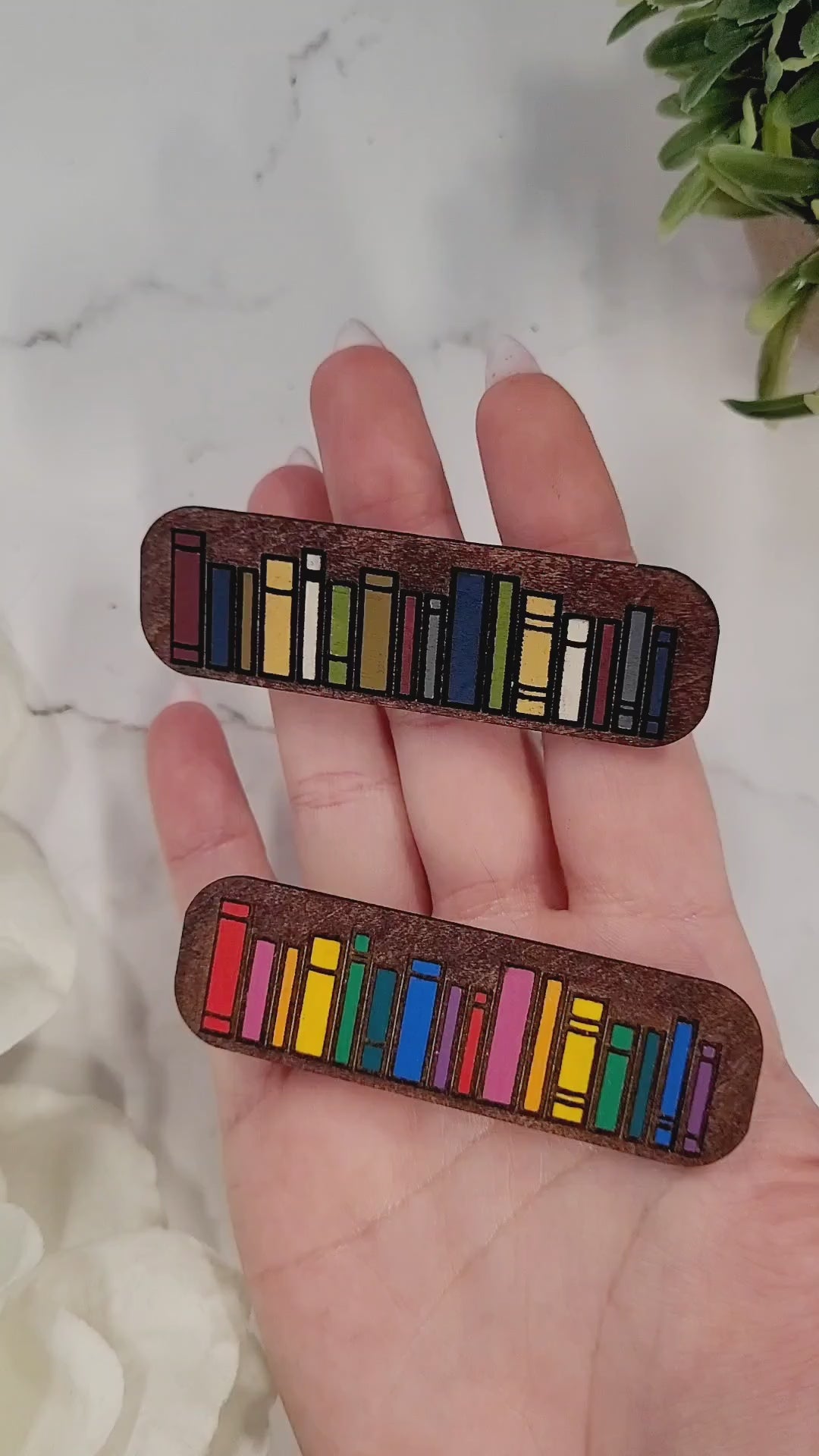 video close up of book hair clips on a white marble background surrounded by foliage.