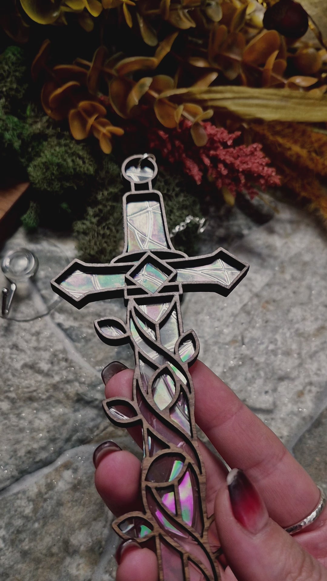video of Enchanted sword suncatcher on a stone background surrounded by foliage 
