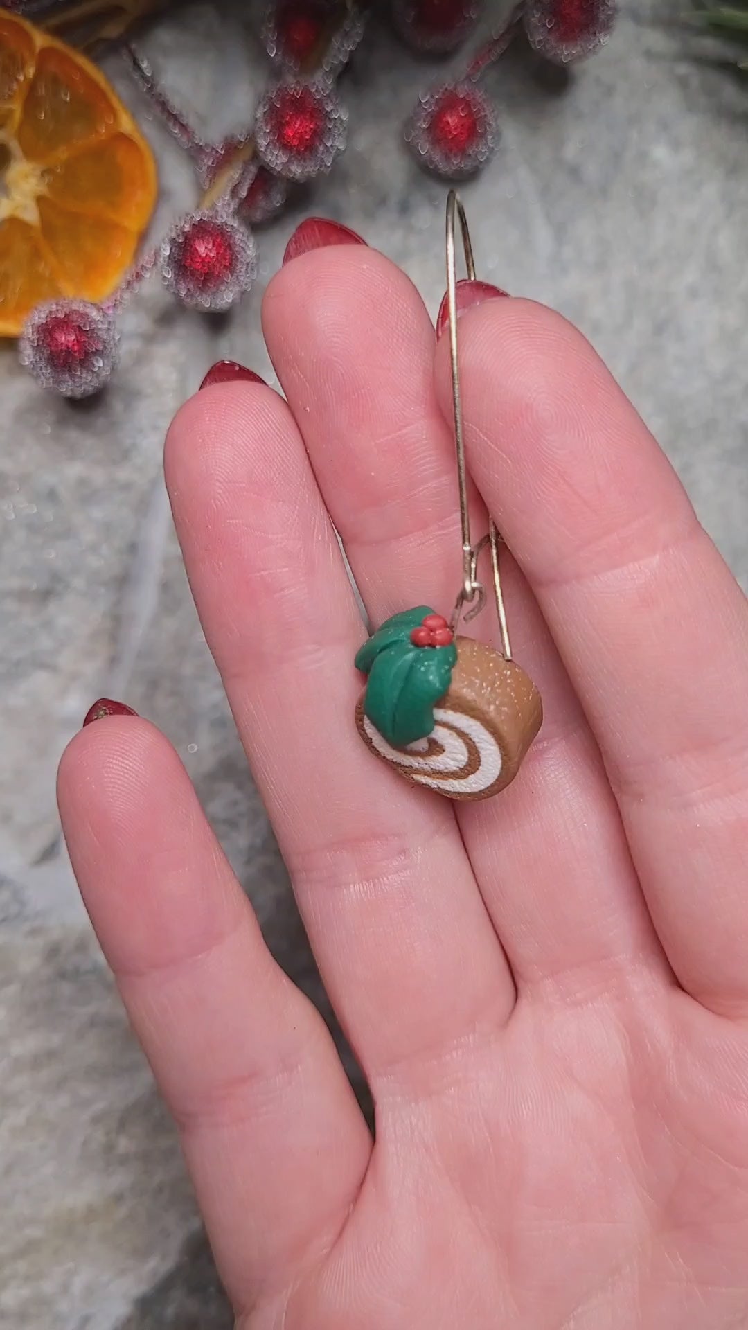 video close up of yule log earrings on a wood and stone background surrounded by foliage. 