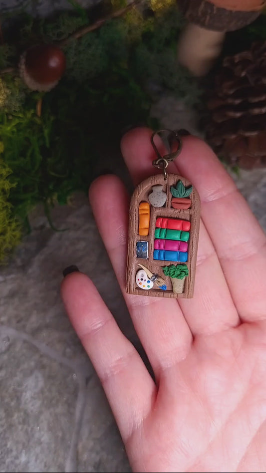 video close up of ACOTAR inspired bookshelf earrings on a stone background surrounded by foliage