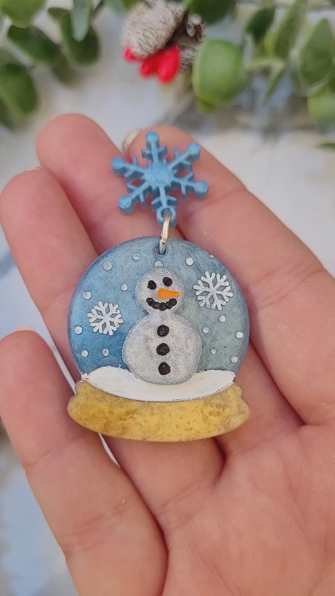 video close up of Snow globe earrings on a marble background with foliage.