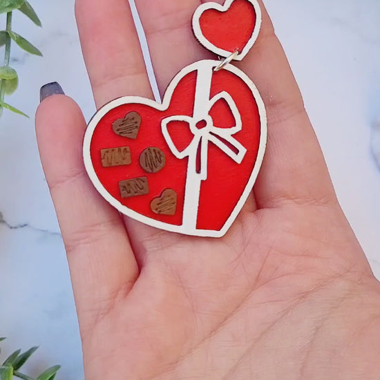 video red and white heart earrings on a white marble background surrounded by foliage.